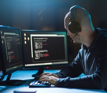 cybercrime, hacking and technology concept - male hacker with headphones and coding on laptop computer screen wiretapping or using computer virus program for cyber attack in dark room