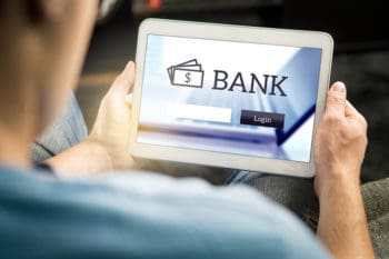 Man using mobile bank application with tablet and smart device at home. Login page to personal account. Online internet banking. Imaginary financial institution website or app.