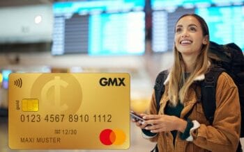 Eine lächelnde Frau mit Rucksack steht in einem Flughafen, während sie ein Smartphone in der Hand hält. Im Vordergrund ist eine goldene Kreditkarte abgebildet, die das Logo einer bekannten Marke zeigt. Hintergrundinformationen zu Karten und Zahlungsverkehr sind relevant.