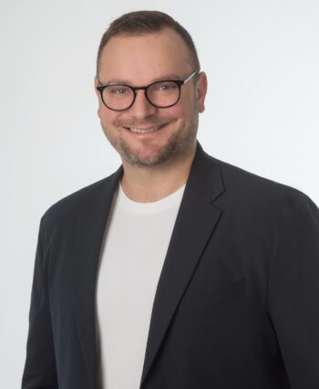 Das Bild zeigt Matthias Bissinger, Senior Security Consultant bei aDvensa. Er trägt einen schwarzen Blazer über einem weißen T-Shirt und lächelt in die Kamera. Der Hintergrund ist neutral und hell. In der Diskussion um LLMs wird betont, dass deren Integration in IT-Umgebungen ohne angemessene Sicherheitskonzepte potenzielle Risiken birgt, da sie oft als Blackbox fungieren und anfällig für Sicherheitslücken sind.
