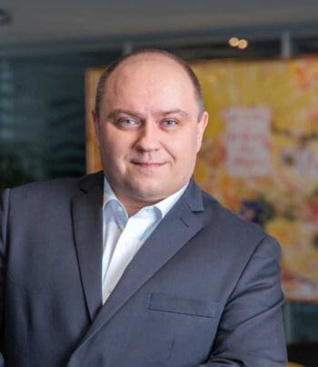 Das Bild zeigt Daniel Fallmann, CEO von Mindbreeze, in einem formellen Anzug. Er steht vor einem farbenfrohen Hintergrund, der eine kreative Atmosphäre vermittelt. Die Mimik ist freundlich und selbstbewusst. In Anbetracht der aktuellen Anforderungen durch DORA wird deutlich, dass effektives ICT-Risikomanagement und die Überwindung von Informationssilos für IT-Abteilungen von zentraler Bedeutung sind, um den neuen regulatorischen Vorgaben gerecht zu werden.