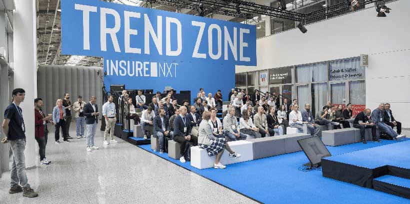 Das Bild zeigt die „Trend Zone“ der InsureNXT 2025, einer Konferenz, die sich auf Innovationen im Versicherungssektor konzentriert. Eine Vielzahl von Teilnehmern ist auf Sitzgelegenheiten versammelt, um den Präsentationen zu folgen. Die Umgebung ist modern gestaltet, mit einem großen, blauen Schriftzug „TREND ZONE“ im Hintergrund. Die Veranstaltung findet in der Koelnmesse statt und fördert den Austausch über KI und wachstumsorientierten Vertrieb.