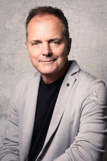 Karl im Brahm, CEO-DACH Objectway: Er trägt einen grauen Blazer über einem schwarzen Oberteil. In der Diskussion um die Unterschiede zwischen traditionellen Banken und Neo-Brokern könnte seine Expertise von Bedeutung sein, da Neo-Broker moderne Technologien nutzen, um effizientere Dienstleistungen anzubieten.