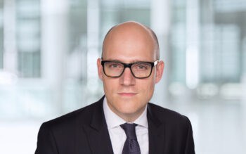 Lukas Henatsch, Director bei KPMG im Bereich Financial Services, präsentiert sich in einem professionellen Umfeld. Seine Expertise umfasst Transformationsprojekte, die auch die Implementierung von Risk-IT in Unternehmen berücksichtigen.