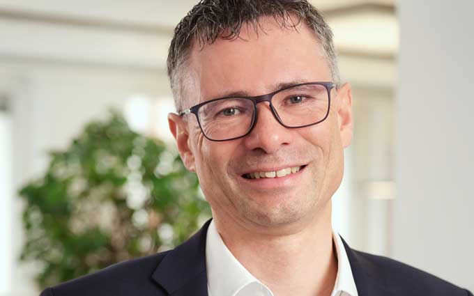 Stephan Schweizer, Chief Executive Officer von Nevis Security, präsentiert sich mit einem freundlichen Lächeln. Der Hintergrund zeigt eine moderne Büroumgebung mit Pflanzen, was auf eine angenehme Arbeitsatmosphäre hinweist. Finanzinstitute stehen vor Herausforderungen durch NIS2.