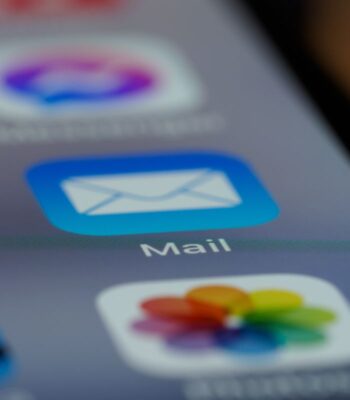 Das Bild zeigt eine Nahaufnahme eines Smartphone-Bildschirms mit verschiedenen App-Symbolen. Im Fokus steht das Symbol für die E-Mail-App, das durch ein blaues Quadrat mit einem weißen Briefumschlag dargestellt wird. Diese Darstellung ist relevant im Kontext der Digital Communications Governance, da E-Mail eine zentrale Rolle in der digitalen Kommunikation spielt. Die Benutzeroberfläche vermittelt einen modernen und benutzerfreundlichen Eindruck.