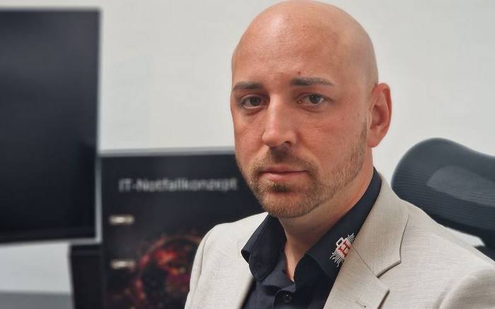 Florian Hansemann, CEO von HanseSecure, thematisiert menschliches Versagen im Kontext der IT-Sicherheit. Im Hintergrund ist ein Plakat zur IT-Nutzersicherheit sichtbar, das die Relevanz des Themas unterstreicht.