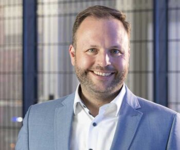Florian Sippel, COO von Noris Network, präsentiert sich lächelnd vor einer modernen Rechenzentrumsumgebung. Die Architektur dieser Einrichtungen steht im Kontext der KI-Revolution, insbesondere im Hinblick auf die Nutzung großer Sprachmodelle (LLMs).