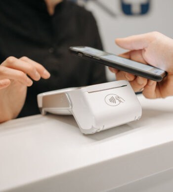 Ein kontaktloses Zahlungsterminal befindet sich auf einer Theke. Eine Person hält ein Smartphone in der Nähe des Terminals, um eine Zahlung durchzuführen. Diese Technologie könnte im Rahmen des EPI zur Verbesserung des Zahlungsverkehrs in Europa beitragen.