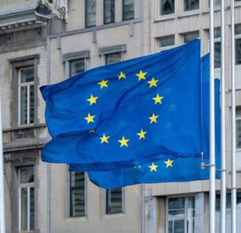 Die Flagge der Europäischen Union weht vor einem modernen Gebäude. Die Einführung der „Verification of Payee“-Regeln zielt darauf ab, Verbraucher besser vor Zahlungsbetrug zu schützen, doch zahlen sollen bei Betrug nur die Banken. Die wehren sich.