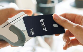 Nahaufnahme einer blauen eToro Visa Debitkarte die an ein Kartenlesegerät gehalten wird.