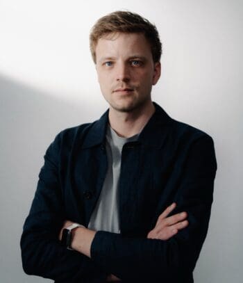 Philipp Hövelmann, Gründer von Cortea, steht mit verschränkten Armen vor einem hellen Hintergrund. Er thematisiert die Herausforderungen der KI im Audit, insbesondere das Blackbox-Risiko.