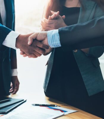 Händedruck zwischen mehreren Personen symbolisiert eine Kooperation im Rahmen des Cash-to-Order-Prozesses. Diese Zusammenarbeit erfolgt zwischen Allianz Trade und Stripe, was auf eine strategische Partnerschaft hinweist. Dokumente und Schreibutensilien sind sichtbar.
