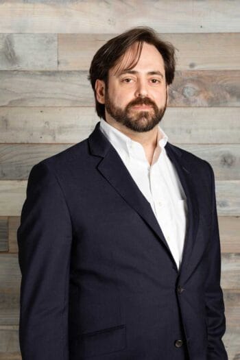 Anders Olson, Senior Manager, Data Science bei Navex, steht vor einer Holzpaneelwand. Seine Präsenz unterstreicht die Bedeutung von Whistleblowing im Kontext aktueller Compliance-Daten, die 1,63 Hinweise pro 100 Mitarbeitende in Finanzinstituten zeigen.