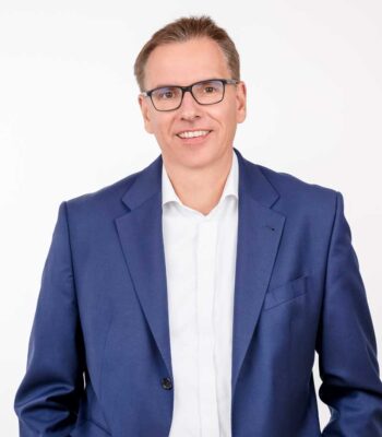 Dr. Stefan Eckhardt, Vorstand der Volksbank Hochsauerland, präsentiert sich in einem formellen Outfit. Die Darstellung unterstreicht die Relevanz von KI in Banken, die eine transformative Rolle in der Finanzbranche einnimmt.