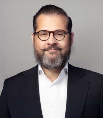 Eric A. Leuer, Manager bei Cofinpro, präsentiert sich in einem formellen Outfit. Sein gepflegtes Erscheinungsbild und der direkte Blick vermitteln Professionalität. In der Diskussion um Prozessoptimierung in der Bank-IT spielt er eine zentrale Rolle.