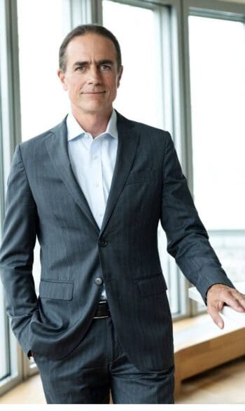 Dr. Raoul Herborg, Managing Director Central Bank Digital Currency (CBDC) bei G+D, präsentiert sich in einem formellen Anzug. Der Hintergrund zeigt große Fenster, die Tageslicht hereinlassen, was eine professionelle Atmosphäre schafft.