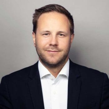 Stefan Söllner, Manager bei Cofinpro, präsentiert sich in formeller Kleidung vor einem neutralen Hintergrund. Seine Mimik vermittelt Selbstbewusstsein und Professionalität, was im Kontext des digitalen Wertpapiergeschäfts von Bedeutung ist.