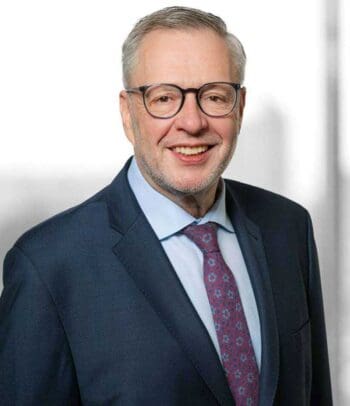 Heinrich Thiele, Rechtsanwalt und Steuerberater bei Baker Tilly, präsentiert sich in formeller Kleidung. Der Kontext des Digitalen Euros wird durch seine Expertise in rechtlichen und steuerlichen Fragen im Bereich digitaler Zahlungsmittel unterstrichen.