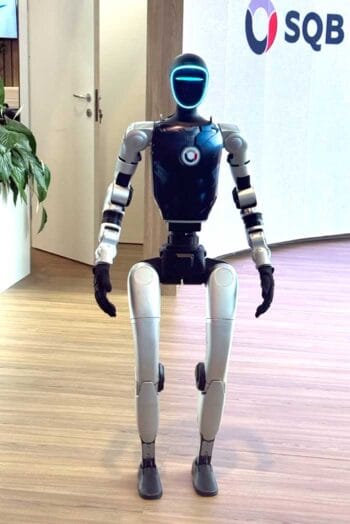 Ein humanoider Roboter steht in einem modernen Ausstellungsraum während der SIBOS 2025 in Frankfurt. Der Roboter hat einen schwarzen Oberkörper und leuchtende Augen, umgeben von einer minimalistischen Umgebung mit Pflanzen und einem Firmenlogo im Hintergrund.