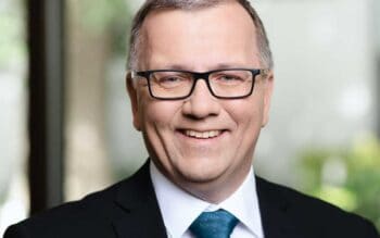Dirk Strauch, verantwortlich für Access Management und Identity Governance bei NTT DATA, präsentiert sich in einem professionellen Umfeld. Excel wird als wichtiges Werkzeug zur Analyse von Zertifikatsrisiken in Banken hervorgehoben.