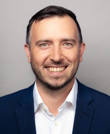 Norman Philipp, Manager bei Cofinpro, präsentiert sich lächelnd in einem formellen Outfit. Die European Digital Identity (EUDI) wird als zukunftsweisendes Legitimationsverfahren hervorgehoben, das über die gesetzlichen Anforderungen hinaus Chancen bietet.