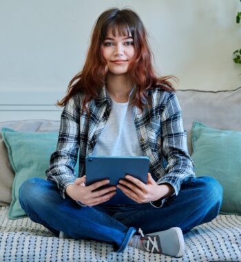 Postbank Bild zur Studie: Junge Frau sitzt im Schneidersitz auf Sofa und hält ein Tablet in den Händen.