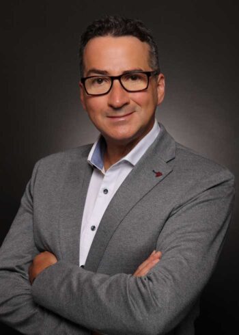 Asdrúbal Pichardo, CEO von Squalify, präsentiert sich in einem grauen Blazer mit verschränkten Armen. Der Hintergrund ist dunkel, was die Professionalität unterstreicht. In der Diskussion um Cyber Risk Quantification (CRQ) spielt seine Expertise eine zentrale Rolle.