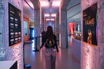 Im Rahmen des Fintech Germany Award 2025 ist ein Veranstaltungsort mit beleuchteten Wänden und Plakaten zu sehen, die die „Hall of Fame“ der vergangenen Jahre präsentieren. Eine Person bewegt sich durch den Raum, der modern gestaltet ist.