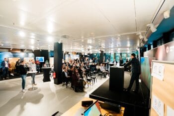 Im FIDA Data Studio präsentieren Fachleute vor einem Publikum innovative Ansätze zu Open Finance. Die Veranstaltung findet in einem modernen Raum statt, der mit Informationsständen ausgestattet ist. Teilnehmer zeigen reges Interesse an den Diskussionen.