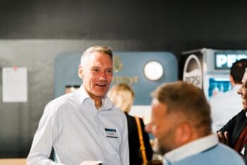 Joris Hensen, Deutsche Bank, steht in einem Gespräch und hält ein Mobilgerät in der Hand. Im Hintergrund sind weitere Personen und ein Verkaufsstand sichtbar. Die Atmosphäre deutet auf eine aktive Diskussion über FIDA und deren Einfluss auf die Datenökonomie hin.