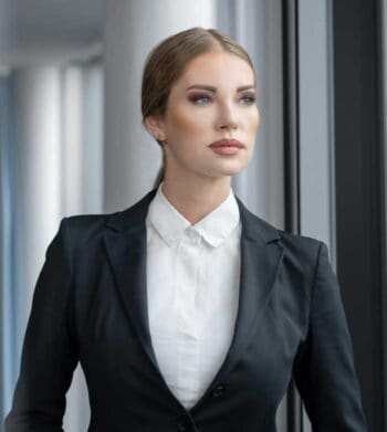 Eine professionell gekleidete Frau steht vor einem Fenster und blickt nachdenklich in die Ferne. Ihr Ausdruck vermittelt Entschlossenheit und Konzentration, was auf die Herausforderungen im Bereich der Zahlungsvorgänge hinweist, die durch neue regulatorische Rahmenbedingungen geprägt sind.