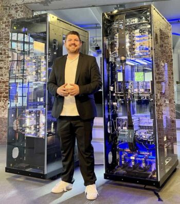 Patrick Hempeler, Leader IBM Z, steht zwischen zwei modernen Mainframe-Systemen. Diese Technologie ist entscheidend für Banken und Versicherungen, um den wachsenden Anforderungen an Sicherheit und den Schutz vor Cyberangriffen gerecht zu werden.