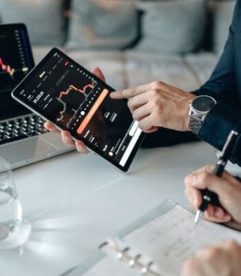 Ein Tablet mit einer Finanzanwendung zeigt Diagramme und Datenanalysen. Eine Person deutet auf die Informationen, während eine andere Notizen macht. Im Hintergrund ist ein Laptop sichtbar. Ant International hat ein KI-Modell zur Prognose von Finanzdaten veröffentlicht.