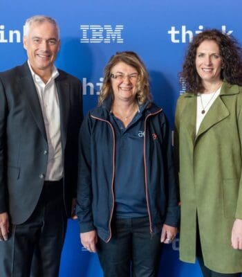 Drei Personen stehen vor einem blauen Hintergrund mit den Logos von IBM und dem Slogan „think“. Die Anwesenden repräsentieren Atruvia und IBM, wobei die Atmosphäre auf eine Zusammenarbeit im Bereich autonomes Banking hinweist.