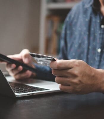 Eine Person nutzt ein mobiles Gerät und eine Kreditkarte, während sie an einem Laptop sitzt. Diese Handlung steht im Kontext der neuen Bezahlmethode von Klarna und der Sparkassen-Finanzgruppe, die digitale Zahlungsoptionen fördert.