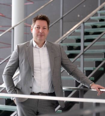 Jens Heilmann, Lead Executive Partner bei msg for banking, steht in einem modernen Gebäude. Die Architektur ist geprägt von klaren Linien und einem offenen Raumkonzept. Der Einsatz von KI im Bankenumfeld wird zunehmend als produktives Werkzeug wahrgenommen.