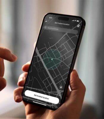 Eine Hand hält ein Smartphone, auf dessen Bildschirm eine Kartenansicht mit der Funktion „Set trusted location“ von Revolut angezeigt wird. Ein grüner Kreis markiert einen bestimmten Bereich auf der Karte.