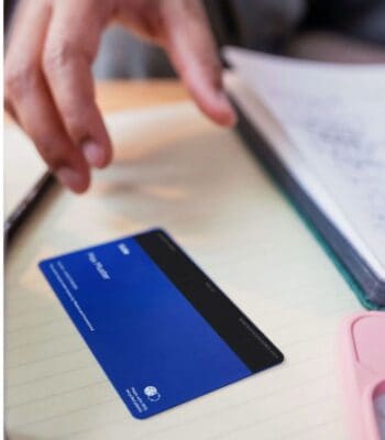 Eine handgehaltene Karte von Tide liegt auf einem Notizblock. Die Karte ist überwiegend blau mit einem schwarzen oberen Bereich und enthält keine sichtbaren Details. Im Hintergrund sind Schreibutensilien und ein Notizbuch erkennbar.