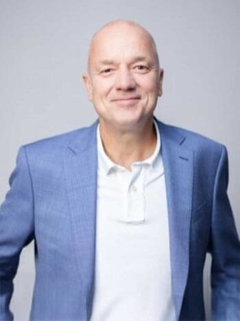 Jörg Dietmann, Mitgründer von Nagarro, präsentiert sich in einem blauen Blazer. Sein Lächeln symbolisiert Optimismus im Kontext der Herausforderungen, die Künstliche Intelligenz im Finanzsektor mit sich bringt, um Werte zu schaffen.