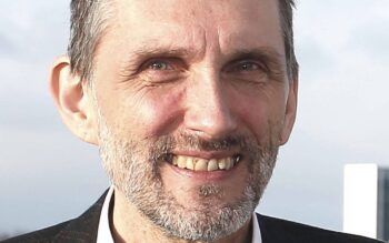 Horst Karaschewski, promovierter Mathematiker und Leiter der Anwendungsentwicklung bei HanseMerkur, präsentiert sich lächelnd. Seine Expertise in der Softwareentwicklung zeigt sich in seiner Rolle, die menschliche Entscheidungsfindung durch KI zu unterstützen.