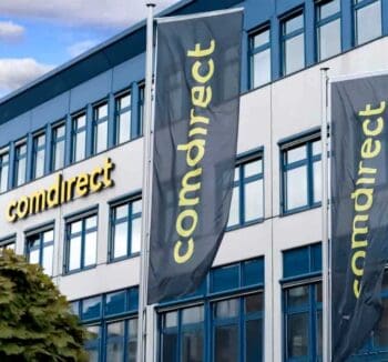 Die Außenansicht des Gebäudes der Comdirect zeigt mehrere Fahnen mit dem Schriftzug „comdirect“. Die Architektur ist modern, mit großen Fenstern und einer klaren Linienführung. Diese Darstellung unterstreicht die Position von Comdirect Pure im Neobroker-Markt.