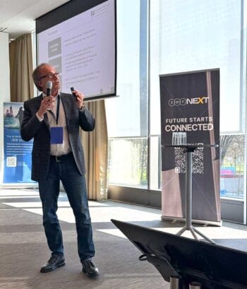 Prof. Dr. Jürgen Moormann der Frankfurt School of Finance & Management präsentiert auf dem International Bankers Forum. Im Hintergrund sind ein Bildschirm und ein Stehtisch sichtbar, während er aktiv Informationen vermittelt.