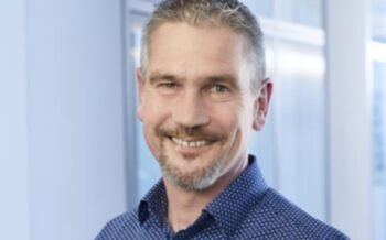 Malte Sukopp, Buildsimple, ist seit über 25 Jahren in der ISR Information Products AG tätig. Er hat verschiedene Positionen als Trainer und IT-Consultant durchlaufen. Der Hintergrund des Bildes zeigt eine moderne Büroumgebung.