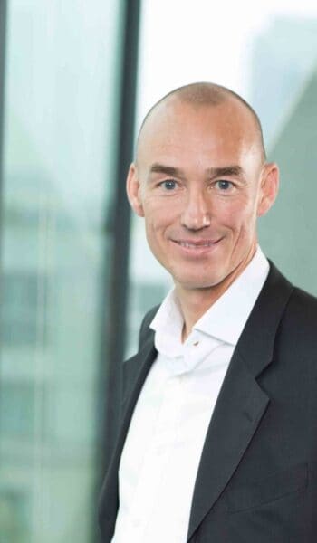 Peter Hiekmann, VP Sales bei finAPI, steht vor einer modernen Architektur. Im Kontext der EU-Verordnung 2024/886 wird die Bedeutung von Instant Payments und der Verification of Payee (VOP) hervorgehoben.