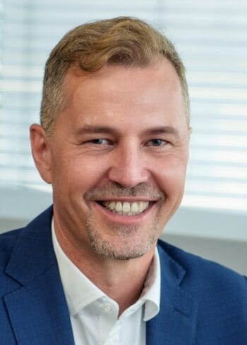 Ralph Weiss, ein Vertreter von BlackLine, wird in einem professionellen Umfeld abgebildet. Sein Lächeln und die formelle Kleidung unterstreichen seine Rolle in der Finanzbranche, die zunehmend von den Fortschritten der künstlichen Intelligenz geprägt ist.