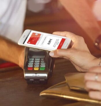 Eine Hand hält ein Smartphone über ein kontaktloses Zahlungsterminal. Auf dem Bildschirm der App ist ein Betrag von 8,99 € sichtbar. Diese Nutzung verdeutlicht die Funktionalität der Sparkassen-App, die im Capital-Ranking führend ist.