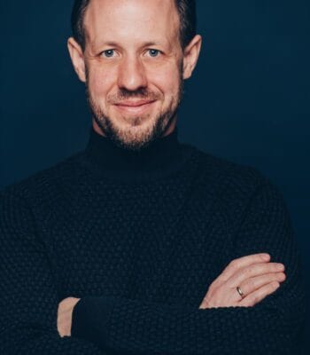 Andreas von Kahlen, Leiter Corporate and Investment Banking bei Capgemini Invent in Deutschland, präsentiert sich in einem schwarzen Pullover vor einem dunklen Hintergrund. Sein Ausdruck vermittelt Selbstbewusstsein und Professionalität, was die Bedeutung von Vertrauen im Finanzsektor unterstreicht.