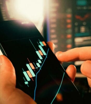 Ein Smartphone zeigt ein Finanzdiagramm mit Kerzencharts, das auf steigende und fallende Kurse hinweist. Diese Darstellung verdeutlicht die wachsende Bedeutung von Nicht-Banken im Firmengeschäft und deren Einfluss auf die Finanzmärkte.