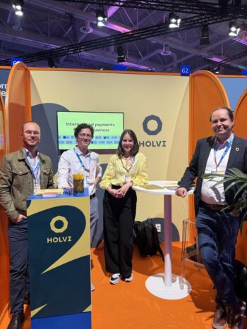 Auf der FIBE 2026 präsentiert Holvi, die FinTech-Bank für Geschäftskonten, ihre Lösungen für internationale Zahlungen. Das Standdesign kombiniert orange und blau, während das Team bereitsteht, um Informationen zu teilen und Networking zu fördern.